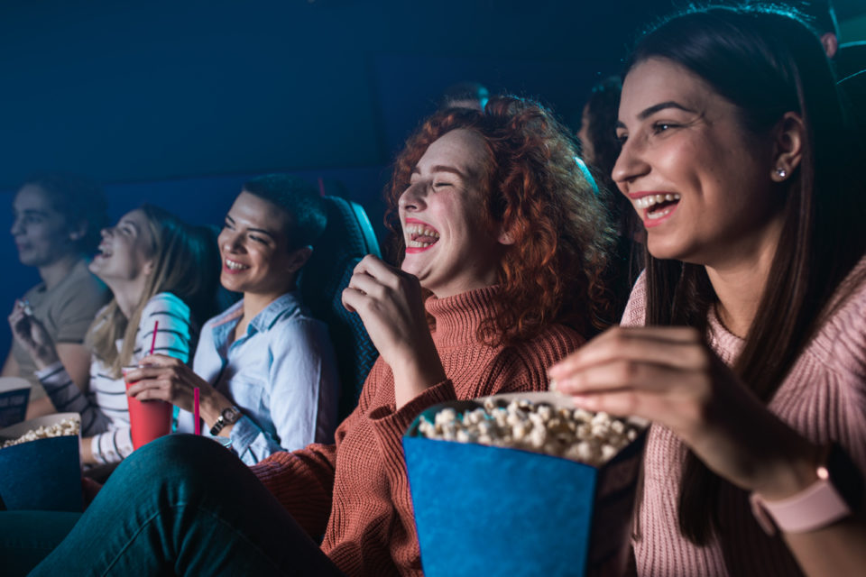 Group of cheerful people laughing while watching movie in cinema.