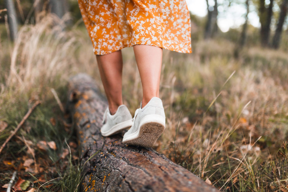 A woman in a dark winter dress walks across a log