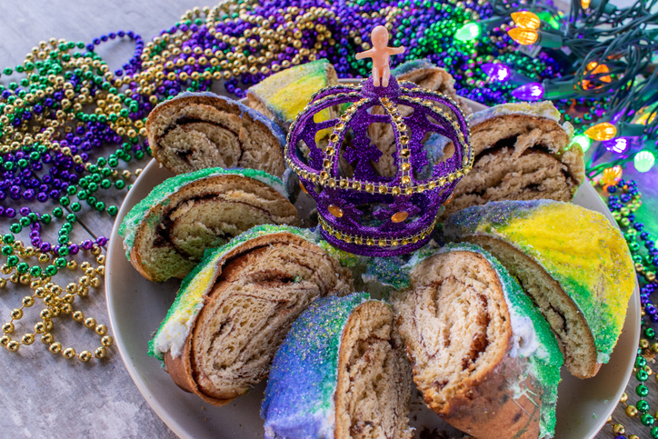 sliced Mardi Gras king cake with baby surrounded by colorful beads