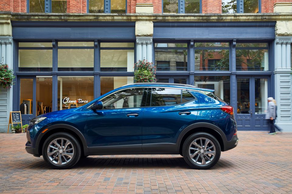 A blue Encore GX SUV n front of a blue store front in a city.