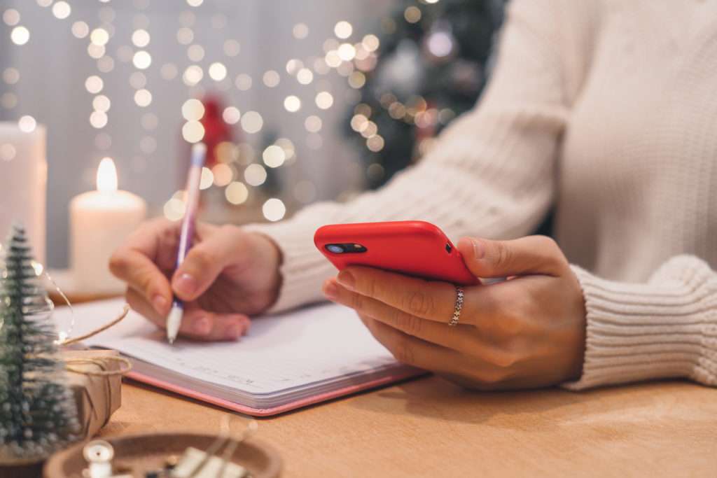 Woman hands with pen and mobile phone writing christmas wish list, goals.